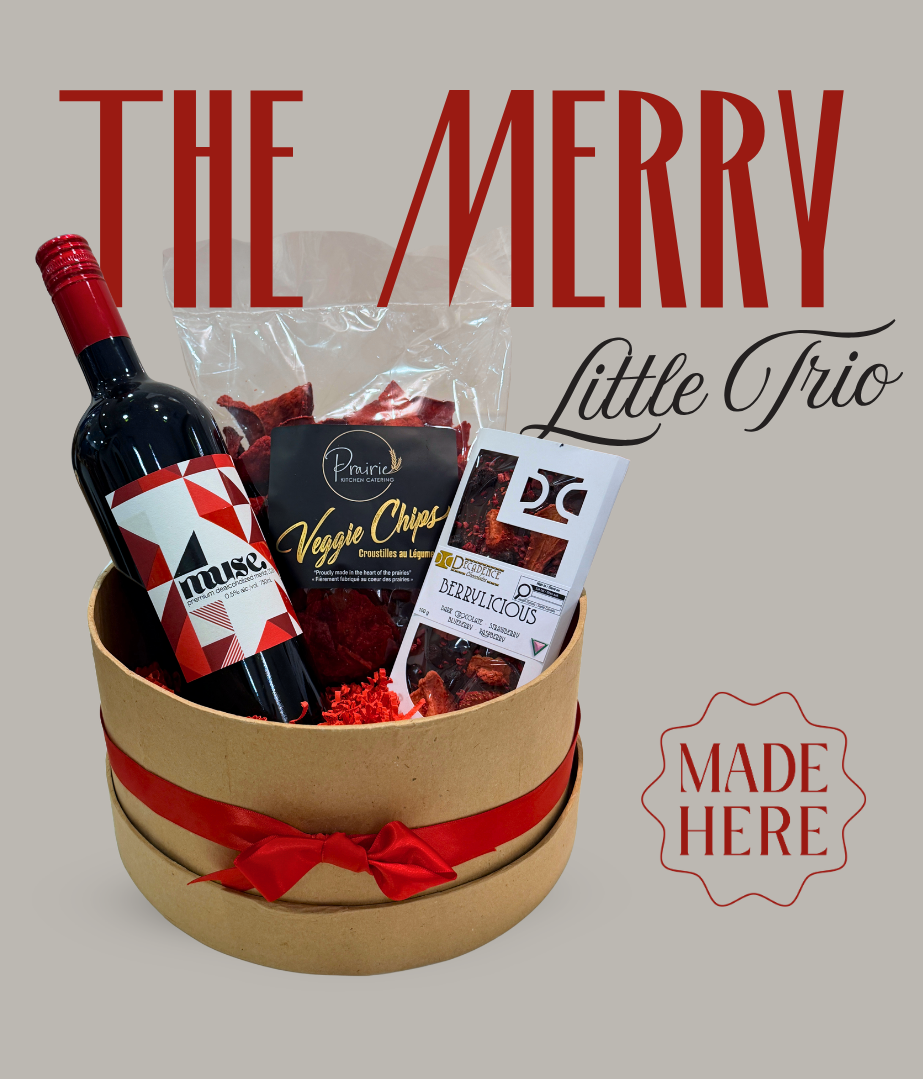 A gift basket set labeled 'THE MERRY Little Trio' containing a bottle of Feudo Rosso red wine, Veggie Chips, and Ferrero Rocher chocolates, presented in a round kraft paper box with a red ribbon, on a solid gray background.