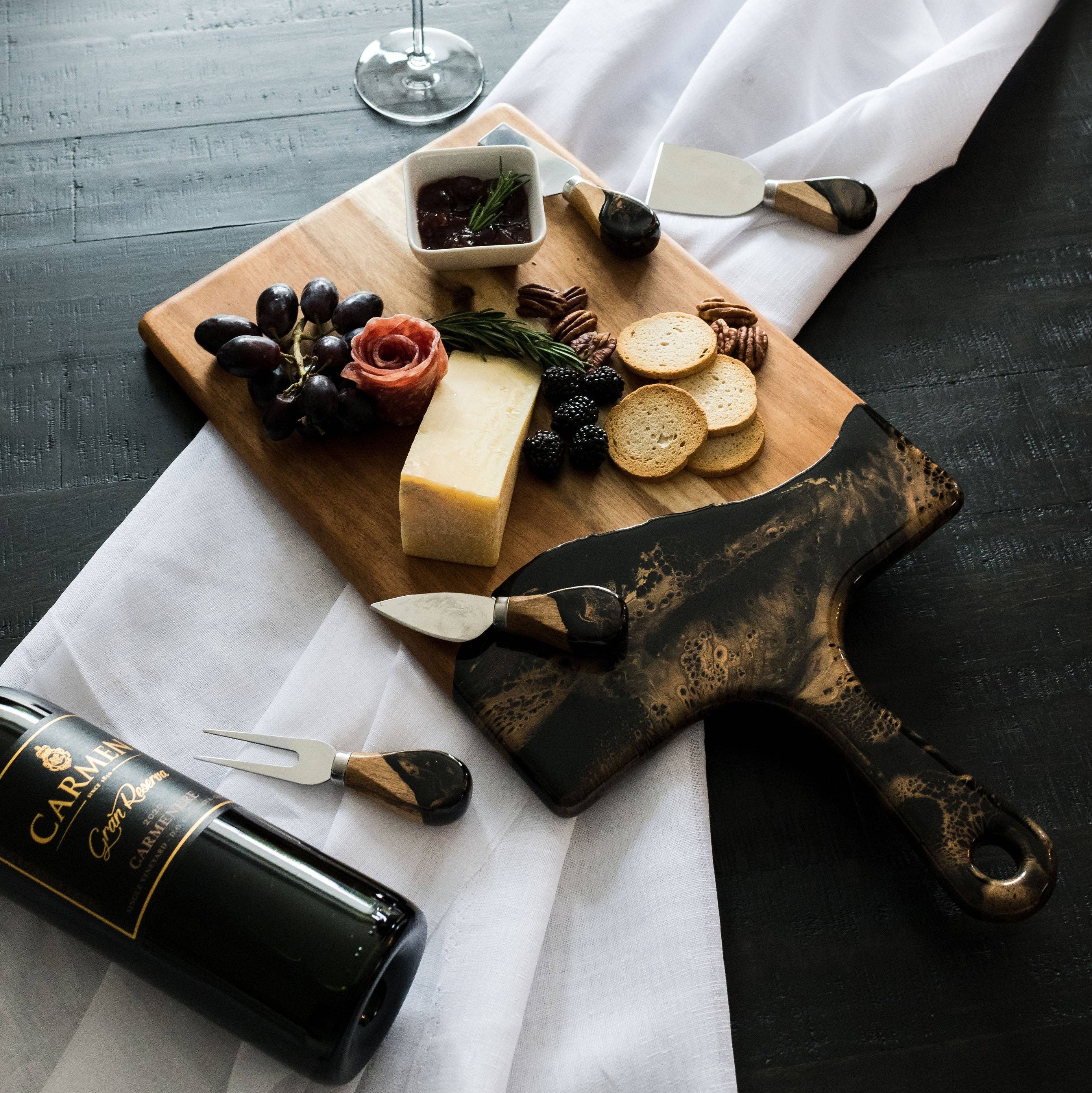 Wooden cutting board with assorted cheeses, fruits, and a bottle of wine on a white cloth.